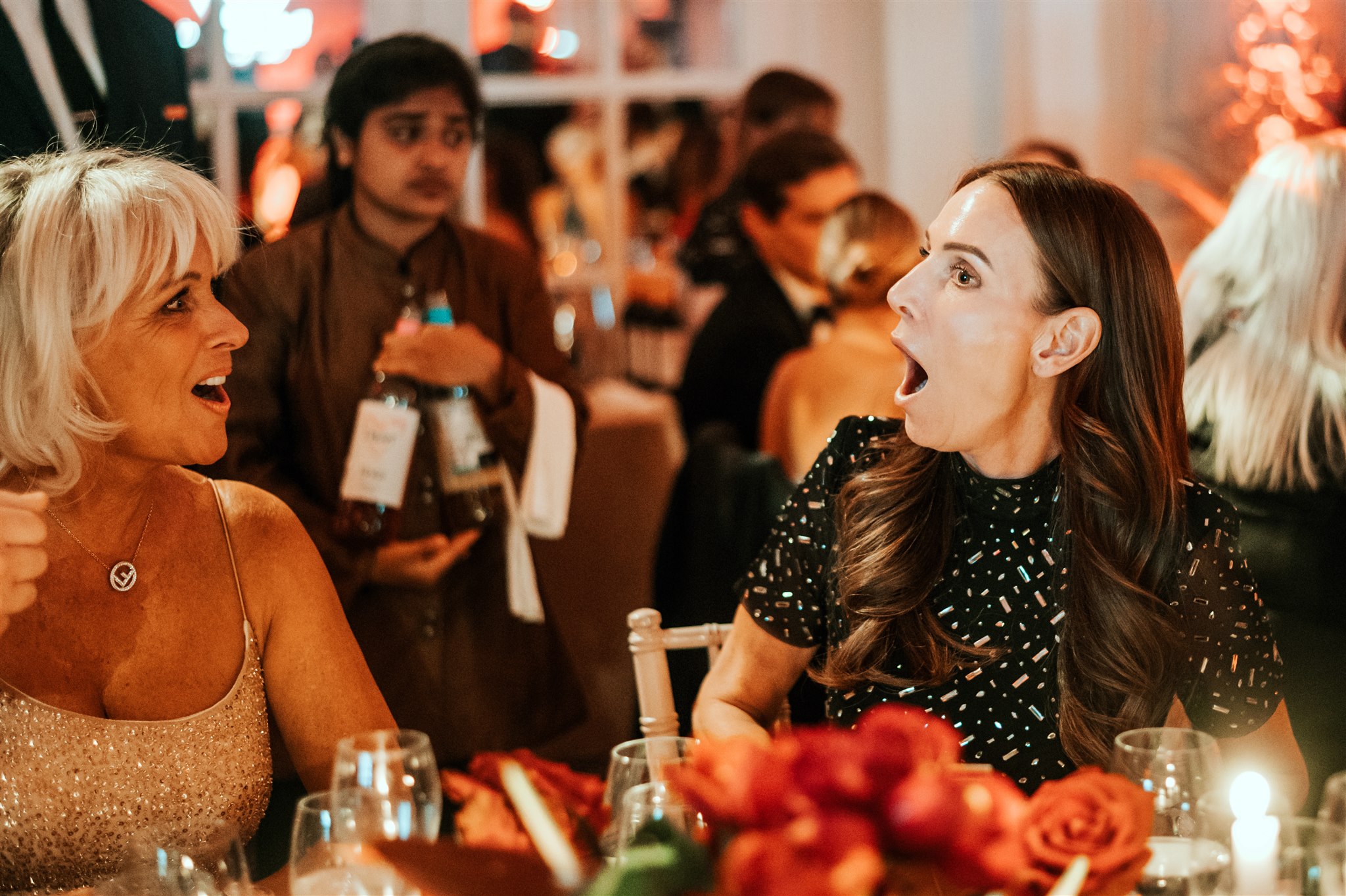 Wedding magician Richard Symes performing close-up magic at a drinks reception, with two female guests reacting in amazement