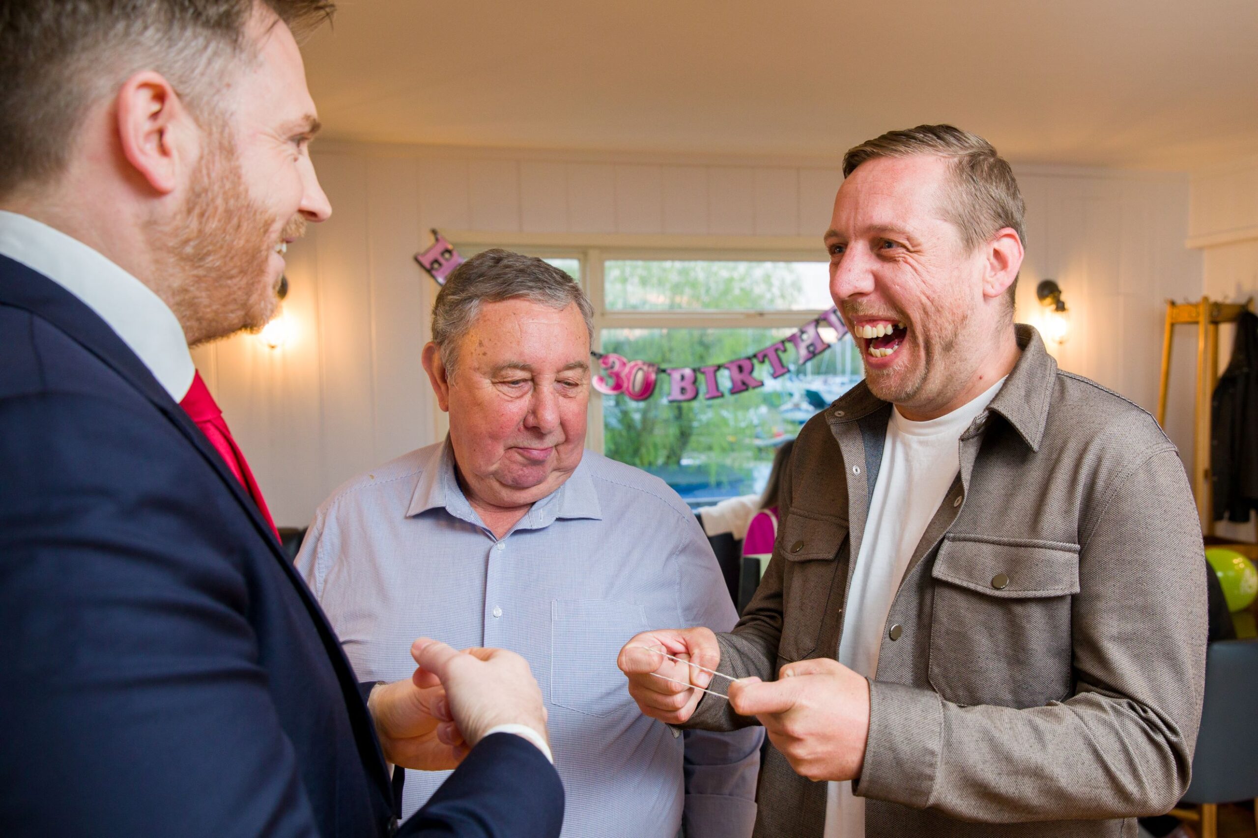 Father and son laughing together while watching a magic trick at a milestone birthday celebration