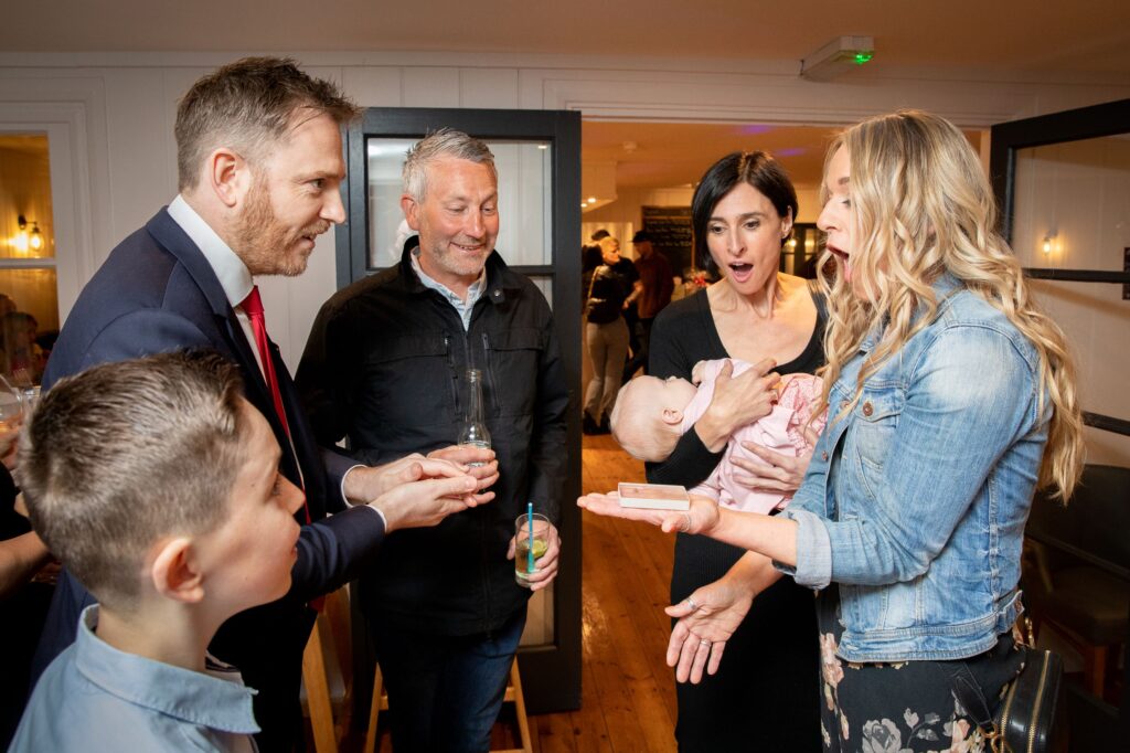 Close up magician performing for adults at a birthday party in Essex with guests of mixed ages reacting in amazement