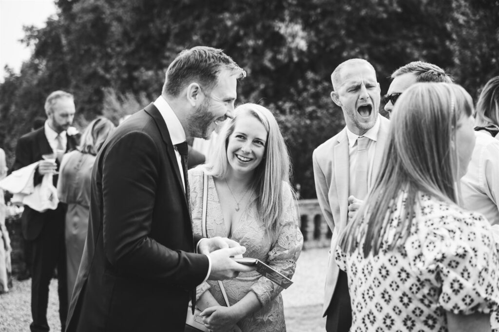 Black and white image of wedding guests laughing during drinks reception magic