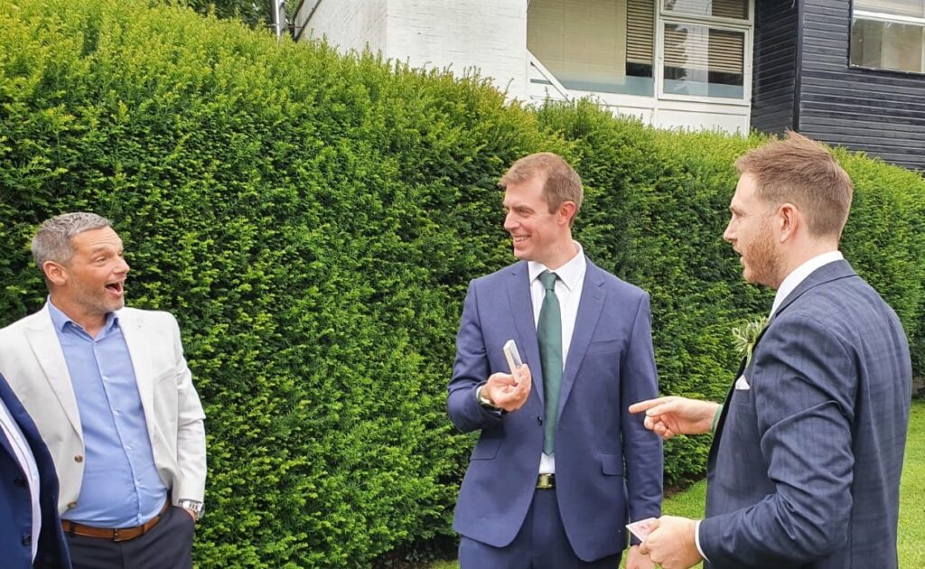 Three wedding guests enjoying close up magic in a garden during afternoon drinks