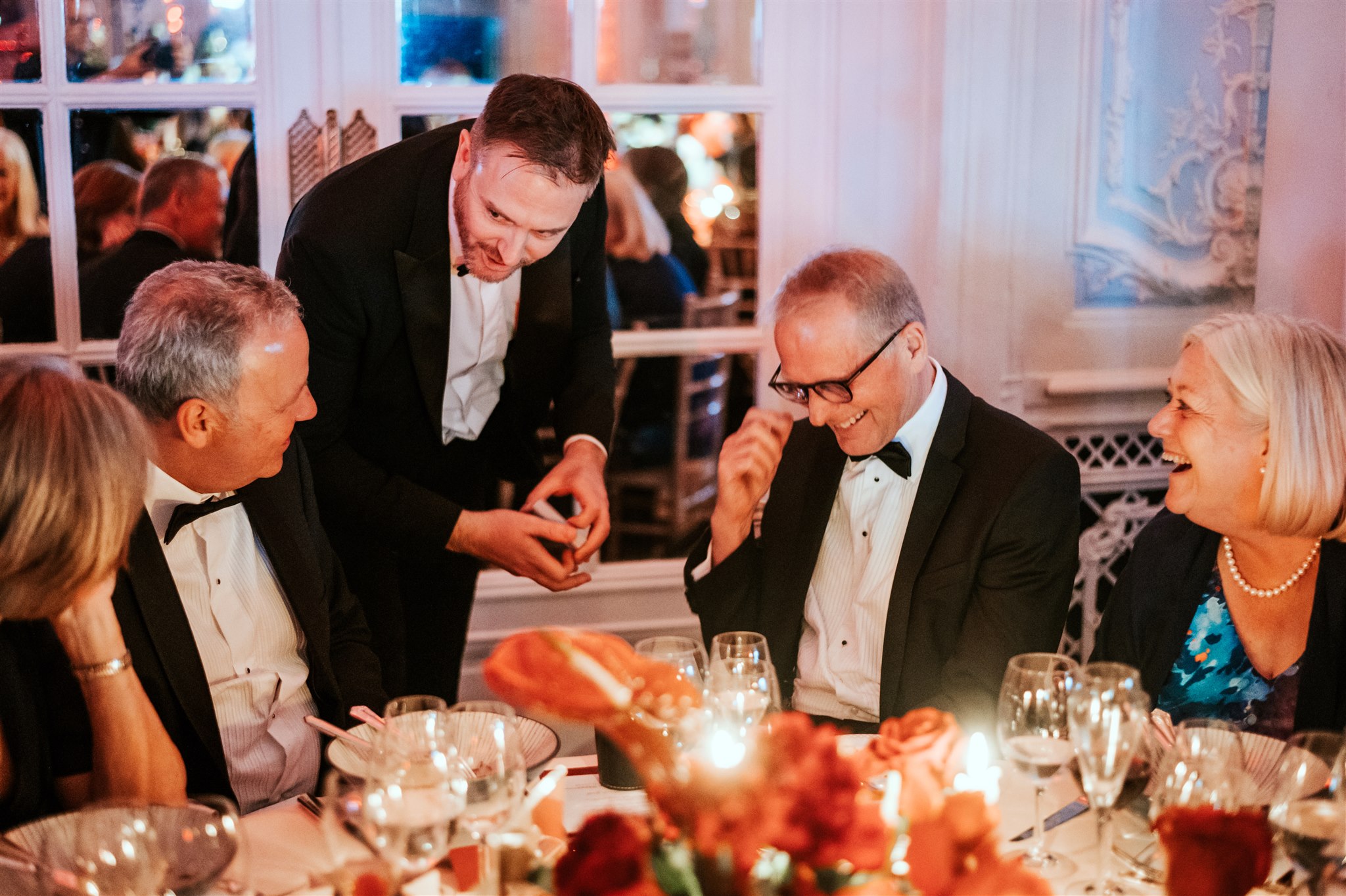 Magician entertaining a small group at a dining table during a milestone birthday celebration