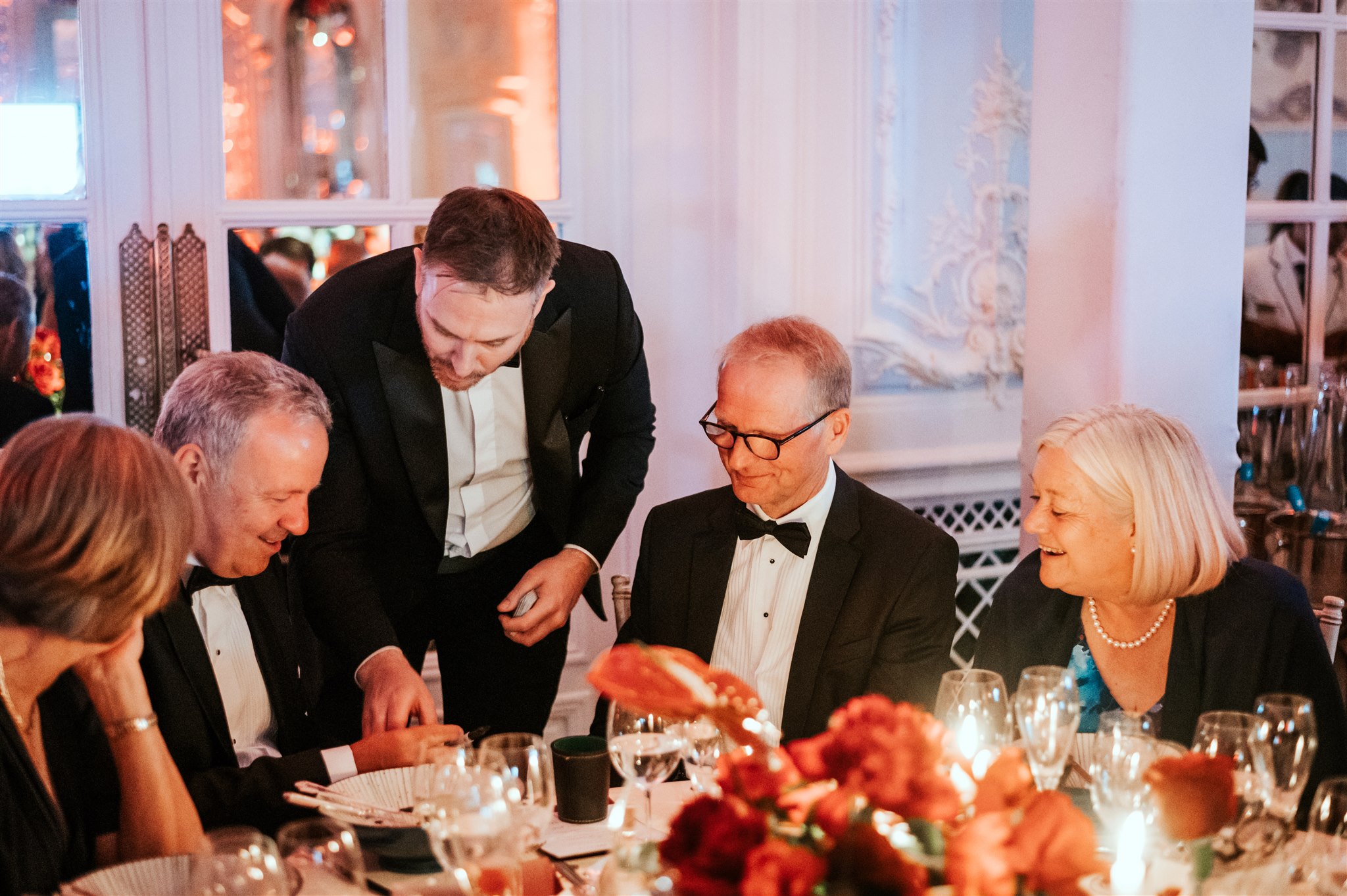 Four guests smiling together during close-up magic at a 60th birthday party