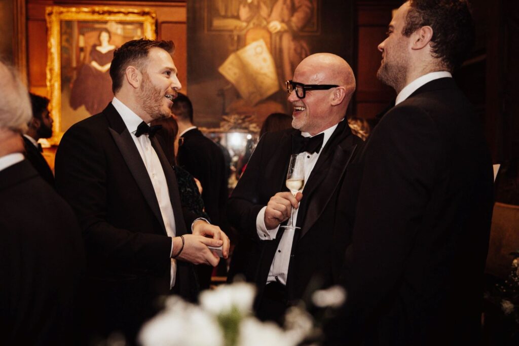 Corporate magician performing card trick for two black tie guests at formal business event