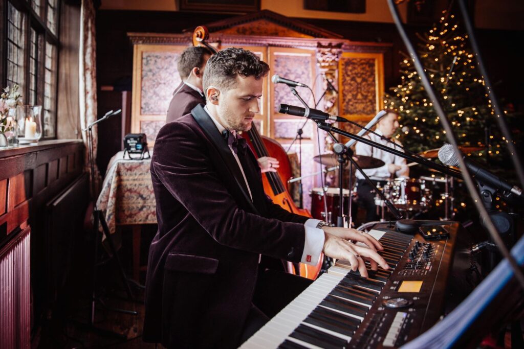 Pianist performing festive music on a piano at a Christmas party with a decorated Christmas tree in the background