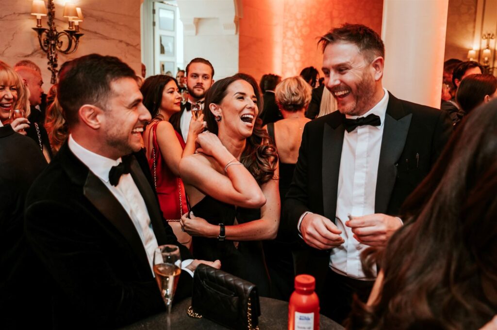 Corporate event guests laughing with close up magician during black tie reception