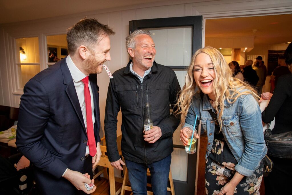 Couple laughing as card reveal ends with magician holding card in his mouth