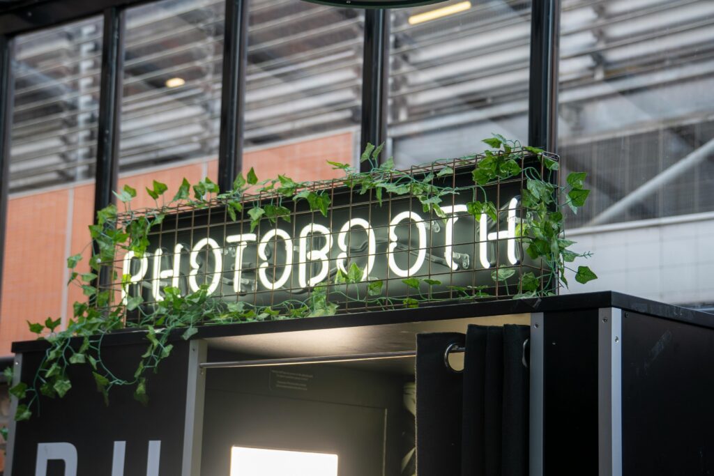 A contemporary photobooth with neon sign and greenery, set outdoors for christmas parties.