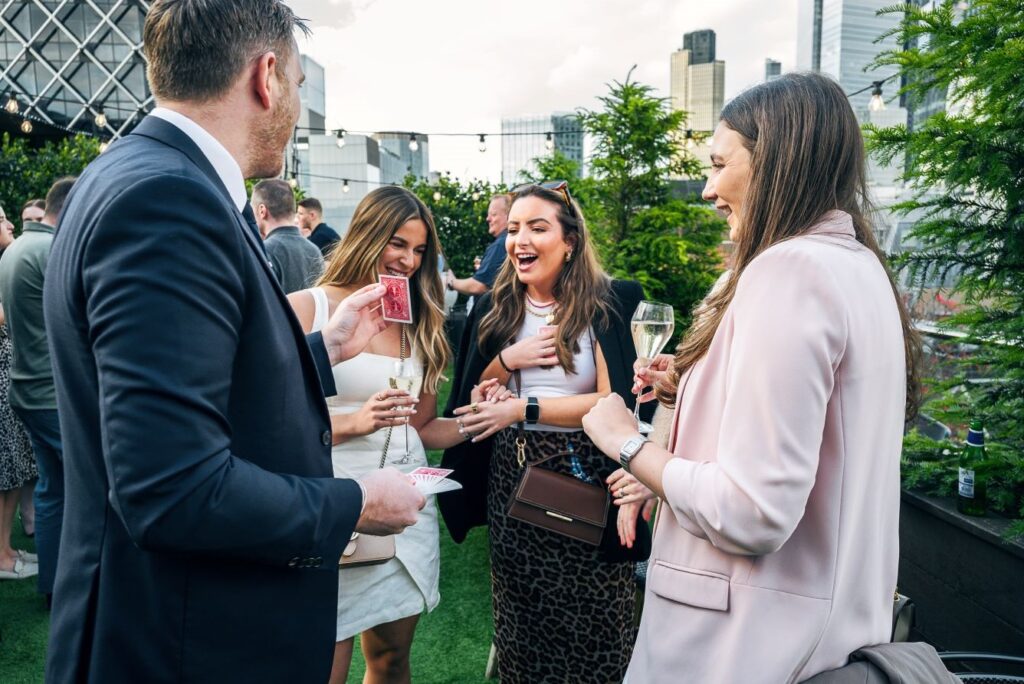 Three guests react to a card trick from summer party magician Richard Symes on a rooftop terrace