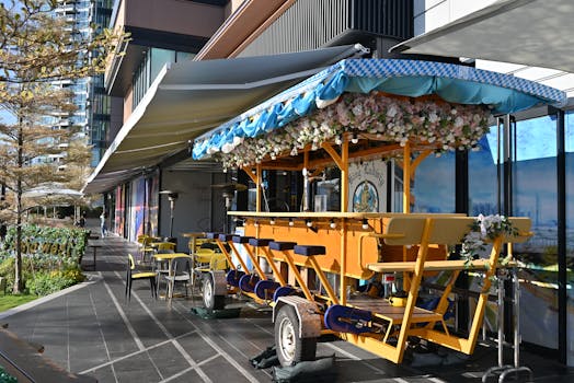 A flower-adorned mobile bar with seating, parked outside a modern city building.