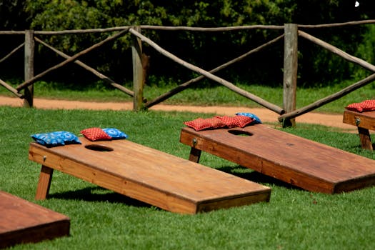 Wooden cornhole boards with colourful bean bags on a green lawn during a sunny day outdoors.