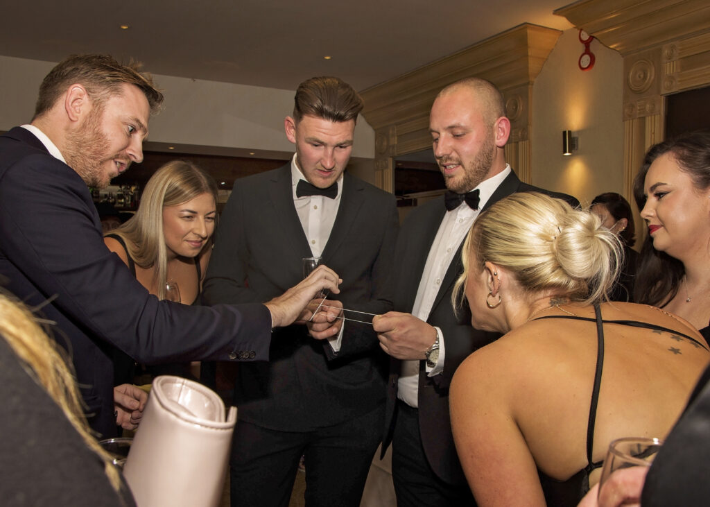 Black tie corporate Christmas event guests leaning in to watch close-up magic