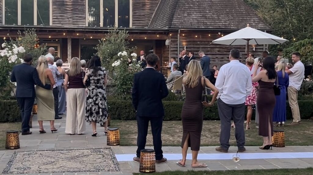 Wedding guests standing and watching the speeches at Houchins in Essex
