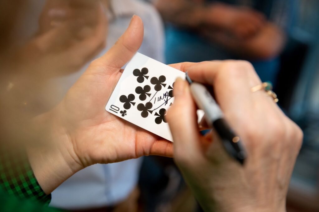 Image of guest writing their name on a playing card close up of pen and card in their hands