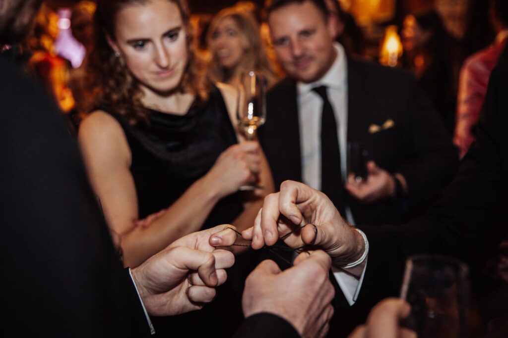 Guests watching closely at a black tie event of an illusion unfolding as a close up magician perfoms at a christmas party